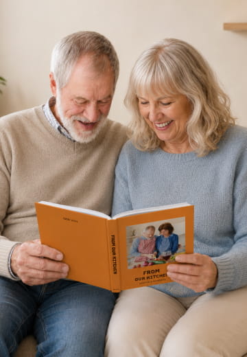 Older couple reading an orange From Our Kitchen cookbook together
