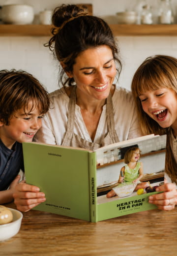Mother and two children laughing over an open Heritage in a Pan cookbook