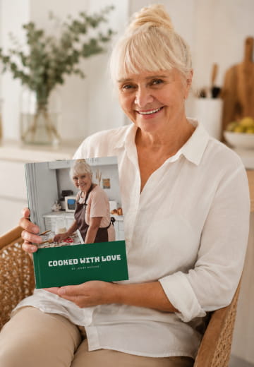 Woman in a white shirt holding a green Cooked with Love cookbook